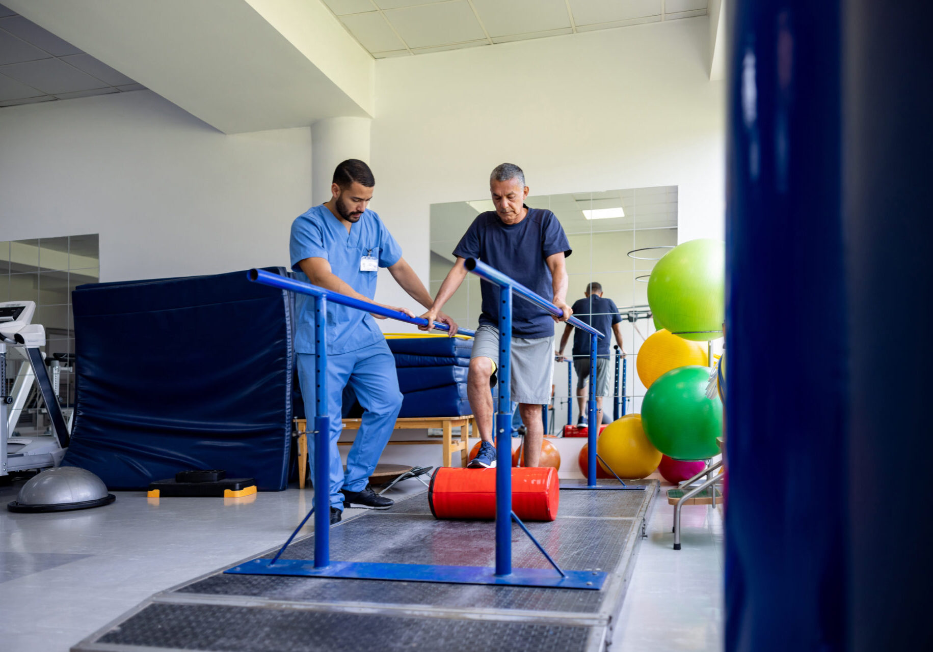 Latin American man doing physical therapy and walking on bars while pushing a roller with his leg